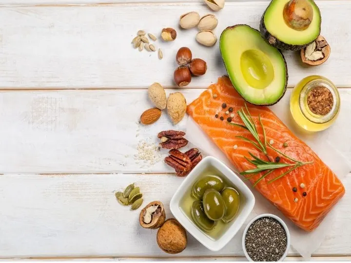 Variety of foods that would fit into Mediterranean Diet including fish, nuts, olives, avocado on a white background.
