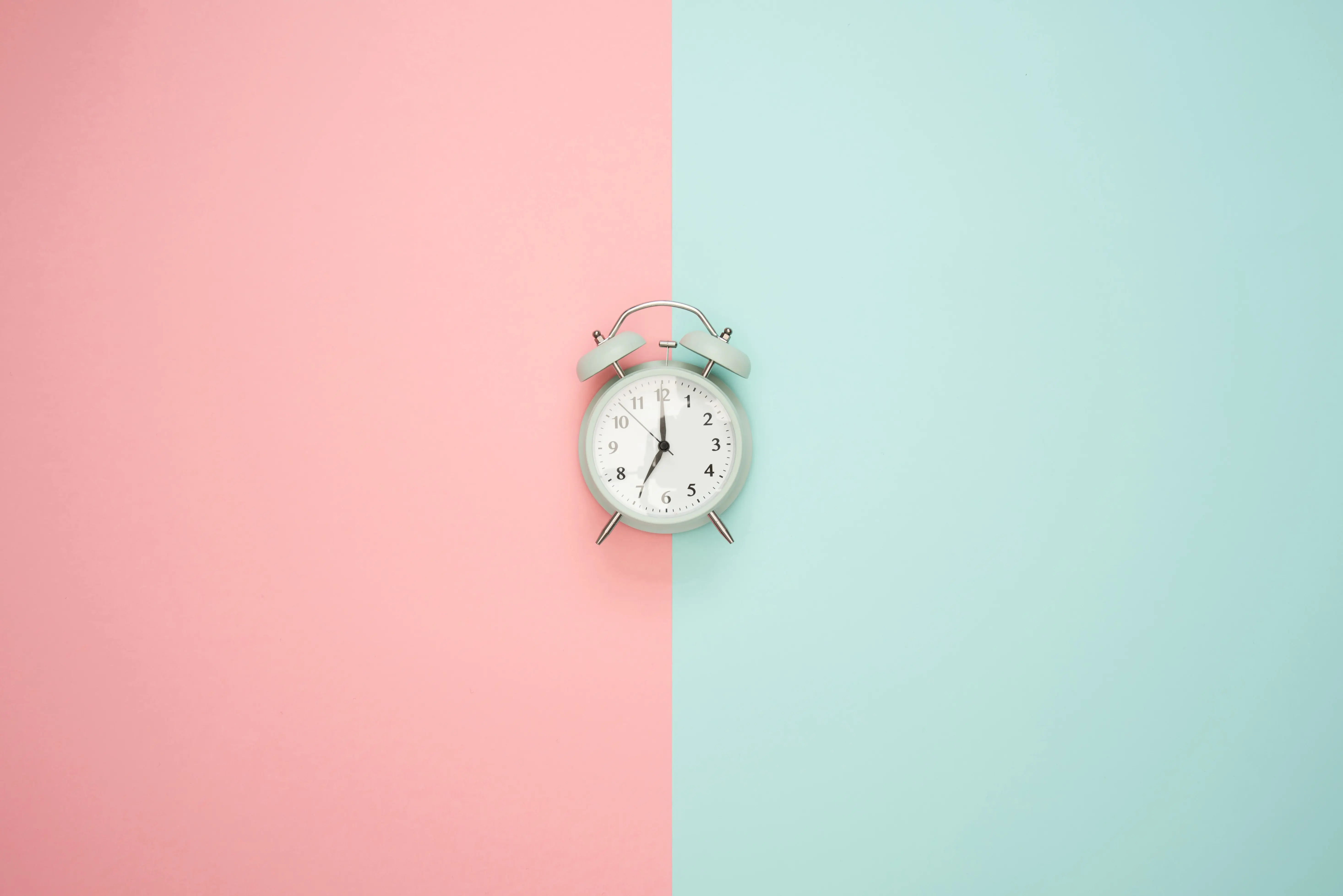 Silver Alarm Clock with background divided in half with pink on left side and green on right side behind clock.