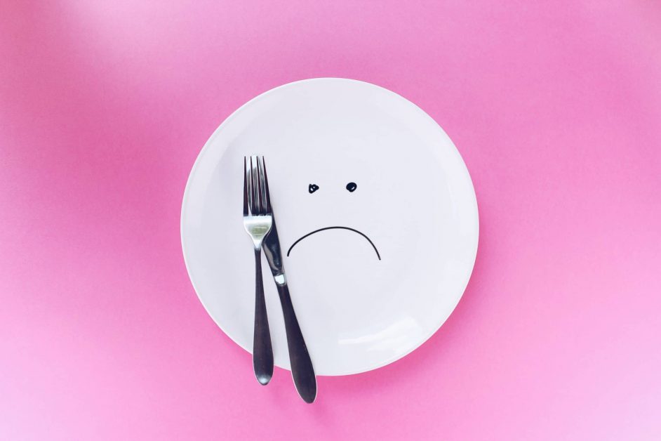 silver fork and knife on empty plate with sad face drawn on plate