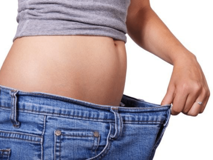 Girl holding blue jeans far from her flat exposed stomach.
