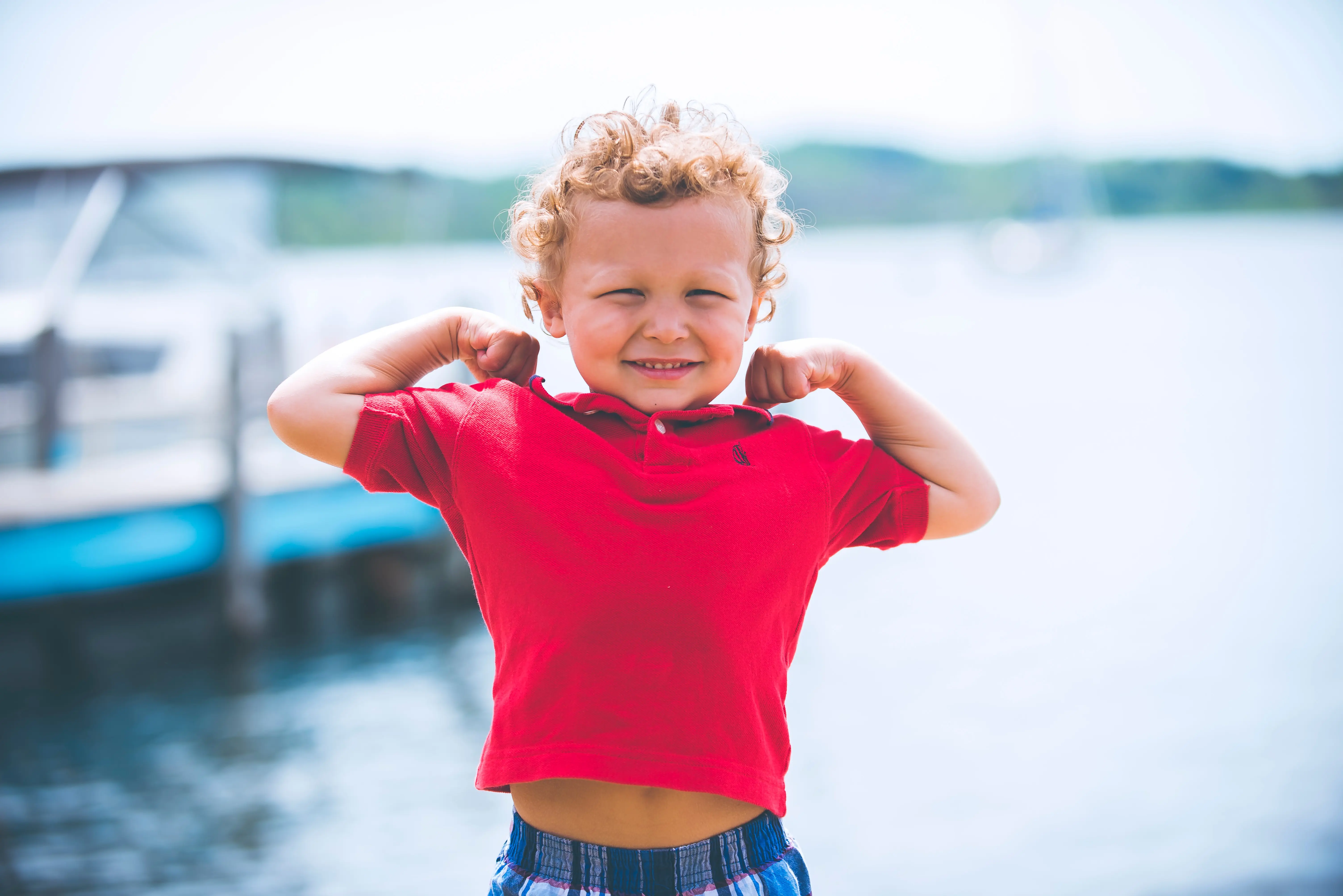 Curly haired boy in red polo standing in front of water.