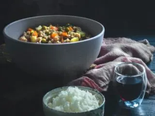 White Ceramic Bowl with White Rice; Gray Bowl with Beans and Vegetables on a Dark Table.