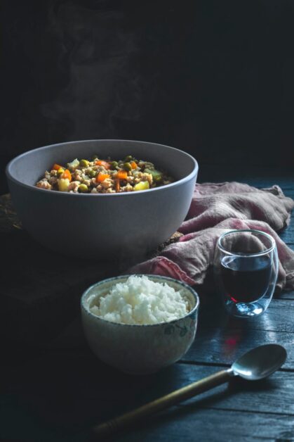White Ceramic Bowl with White Rice; Gray Bowl with Beans and Vegetables on a Dark Table.