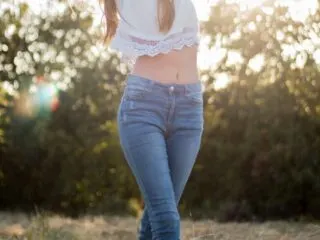 Woman Wearing White Crop Top in Blue Jeans in Field with sun behind her.