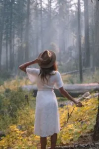 Woman in White Short Sleeved Dress Standing in Forest Basking in Sunlight