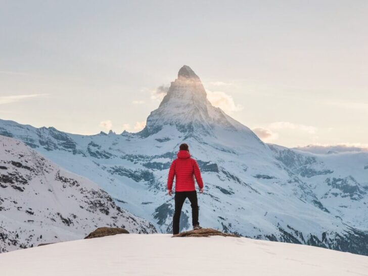 Guy Standing At Edge of Cliff in Snow Looking at Mountain In Distance