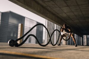 Guy in Grey Shirt Doing Battle Ropes with Kettlebell as Anchor