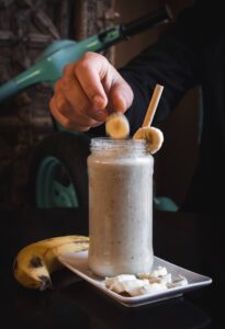 Person Putting Sliced Banana in Smoothie Glass Jar