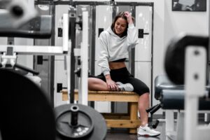 Woman Waring White Sweatshirt Smiling Sitting on Bench in Gym