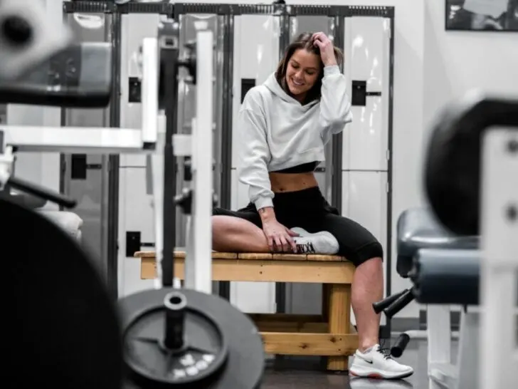 Woman Waring White Sweatshirt Smiling Sitting on Bench in Gym