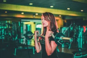 Woman Using Curl Barbell to Perform Bicep Curl in Gym