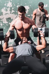 Guy Doing Dumbbell Bench Press with Spotter While Straining To Complete Movement