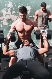 Guy Doing Dumbbell Bench Press with Spotter While Straining To Complete Movement