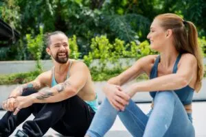Man and Woman In Workout Clothes Sitting Next To Each Other Smiling