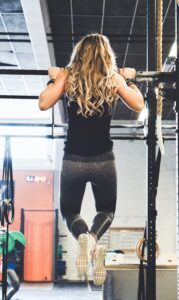 Woman at Top of Pull Up Movement in Gym