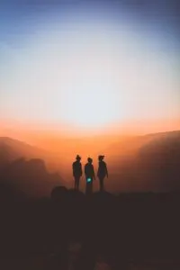 Three Friends Standing on Cliff With Sunsetting Behind