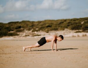 Guy Doing Burpee With Shirt Off On Beach