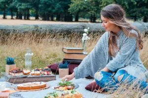 Woman Sitting on Blanket Eating Picnic in Field