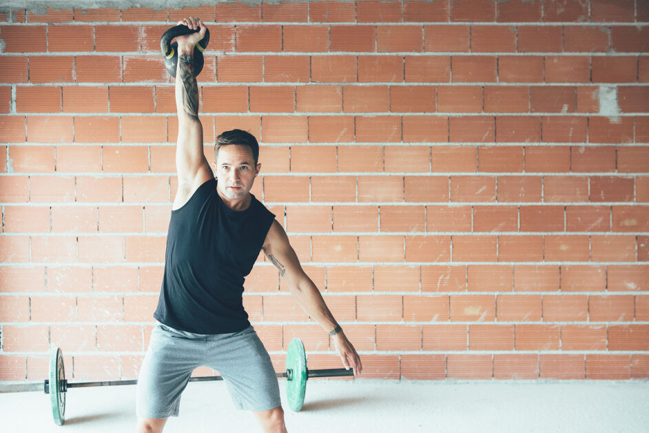 Fitness Young Man Doing A Weight Training By Lifting Kettlebell