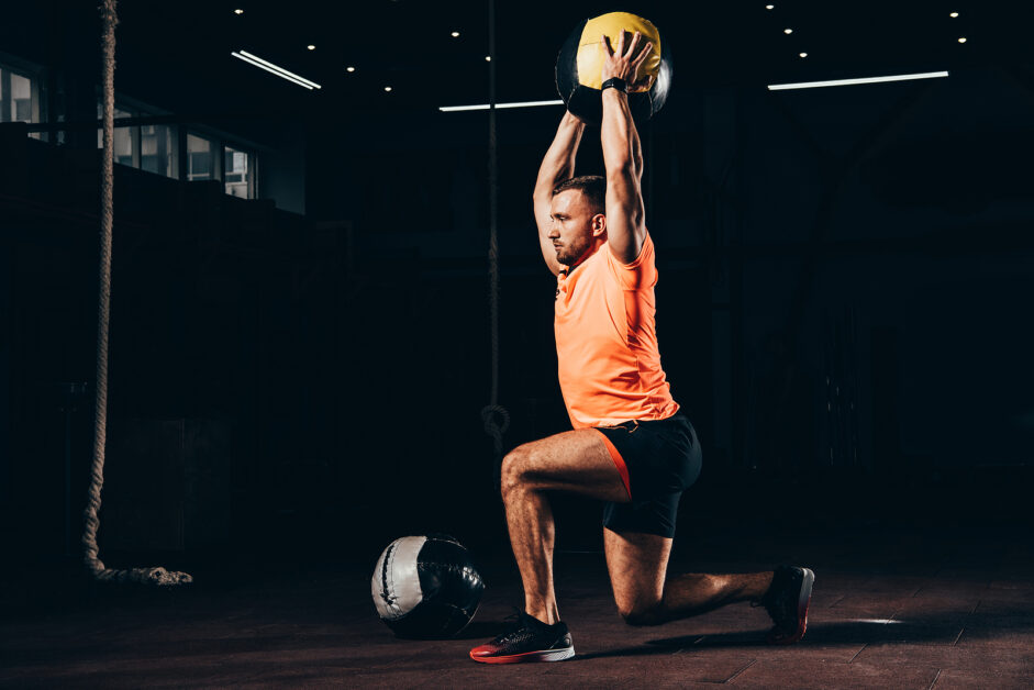 Handsome Fit Sportsman Performing Lunge With Medicine Ball Overh