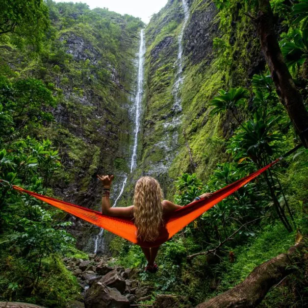 Woman resting in red hammock in front of waterfall.