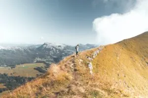 Man standing on ridge of mountain with clouds in the background.