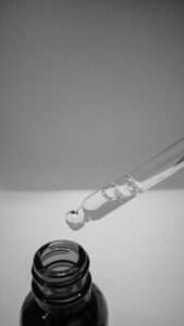 Bottle of serum and dropped with serum in the glass tube on a grey background