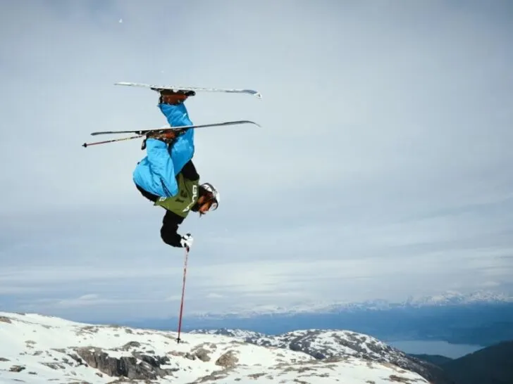 Skier in blue jacket doing flip off a jump using flow state.