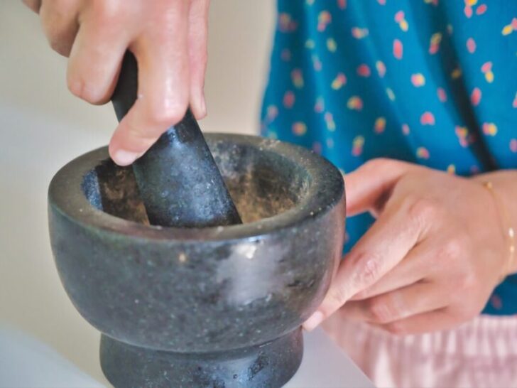 Woman using grey mortar and pestle to grind herbs.