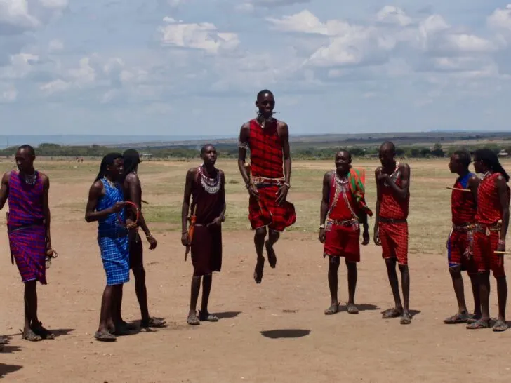 Massai warriors standing in semi-circle with one doing ceremonial dance.