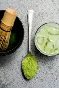 Spoon with green powder next to glass with ice.